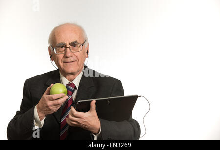 old senior businessman working with black tablet computer, wearing business suit, eating apple Stock Photo