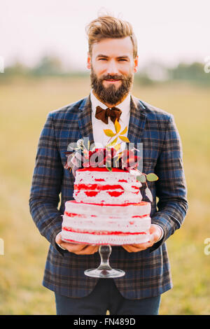 Stylish bearded groom with delicious wedding cake in hands Stock Photo