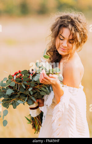 Lovely bride in white dress holds bouquet  and softly smiling Stock Photo