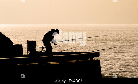 Silhouette of man fishing in sea from jetty against monotone background. Stock Photo