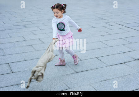 Happy three year old girl playing with her coat in the city. Selective focus Stock Photo