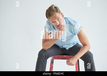 Brutal man in a shirt with short sleeves sitting in the chair , his fists clenched , slightly bent , under the gaze of the foreh Stock Photo