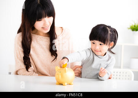 Happy mother and daughter Inserting Coin In Piggy bank Stock Photo