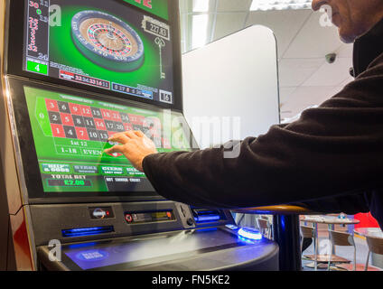 Mature man using fixed odds Roulette machine (FOBT fixed odds betting terminal) in Bookmakers. England, UK Stock Photo