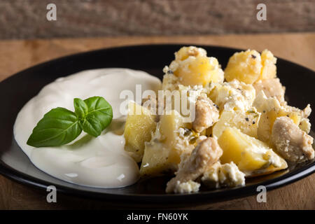 Potatoes gratin with sour cream and chicken meat fried in butter on wooden background Stock Photo