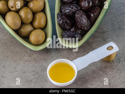 Green and black salted olives and measuring spoon with olive oil on textured background Stock Photo