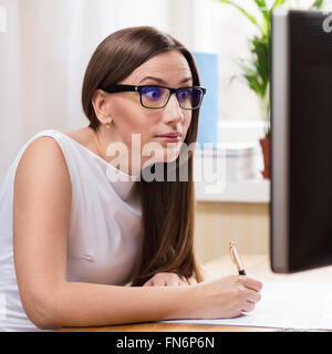 Surprised businesswoman in white dress and glasses reading from monitor Stock Photo