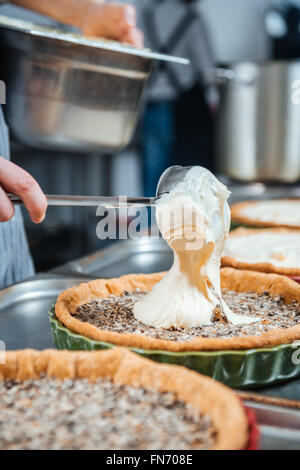 Chief cook in process of cooking several pies with cream on the kitchen Stock Photo