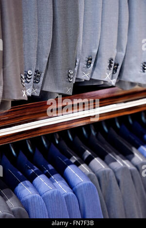 Elegant blue and gray suits on hangers are seen in a suit store Stock Photo