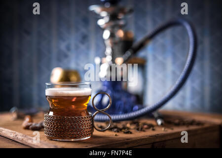 Black tea in glass cup on wooden table, hookah in background Stock Photo