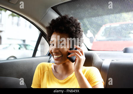 Close up portrait of smiling young african woman sitting in back seat of a car talking on mobile phone Stock Photo