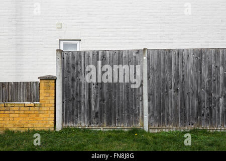 View of a house from the road, with grey wooden fence and yellow brick wall. Stock Photo