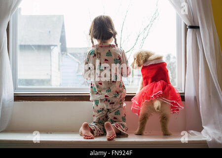 Girl in pyjamas looking out the window with golden retriever puppy dog Stock Photo