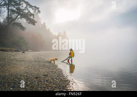 Boy and golden retriever puppy dog playing with stick in the ocean Stock Photo