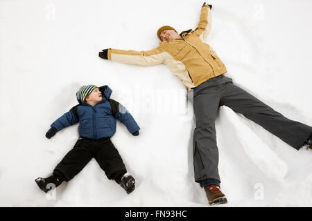 Two people, a man and a child lying in the snow make snow angel shapes. Stock Photo