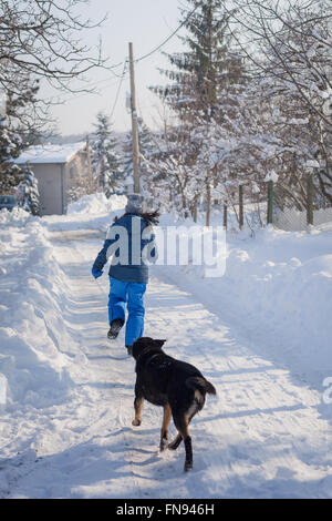 Dog chasing woman down the street in snow Stock Photo