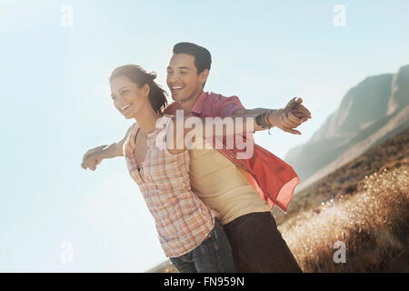 A couple standing close together, arms outstretched leaning into the breeze, in open country. Stock Photo