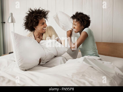 A young couple sitting in bed, playfighting with pillows. Stock Photo