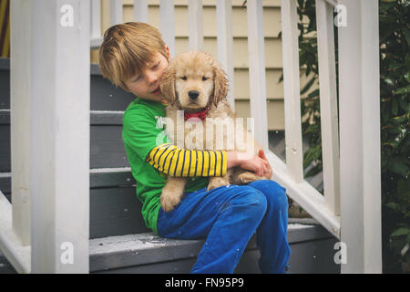 Boy sitting on patio steps with golden retriever puppy dog Stock Photo