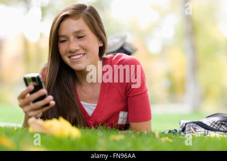 A girl lying on the grass using a mobile phone. Stock Photo