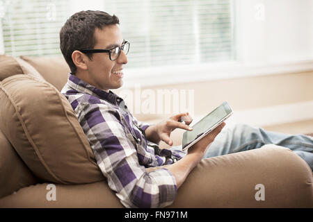 A man sitting on a sofa, using a touchscreen digital tablet. Stock Photo