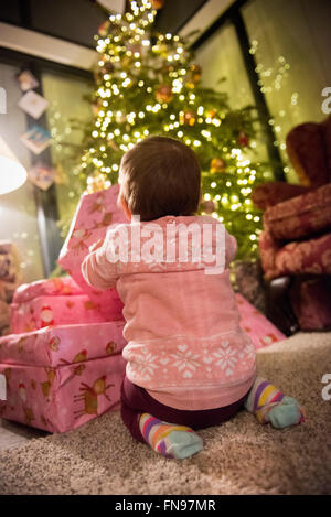 A toddler beside a pile of presents under a Christmas tree. Stock Photo