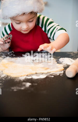 A boy in a Santa hat making Christmas biscuits, cutting out shapes. Stock Photo