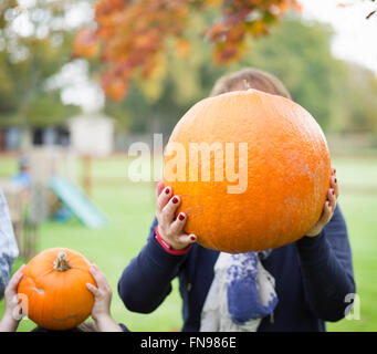 A woman and a child holding pumpkins in front of their faces. Stock Photo
