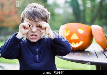 A boy looking through his curved fingers beside a carved pumpkin lantern, Stock Photo