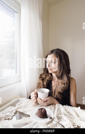 Young woman sitting with cup of tea and chocolate dessert Stock Photo