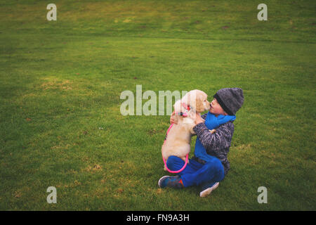 Boy kissing his golden retriever puppy dog Stock Photo