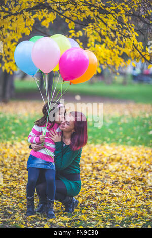 Girl holding balloons kissing her mother Stock Photo