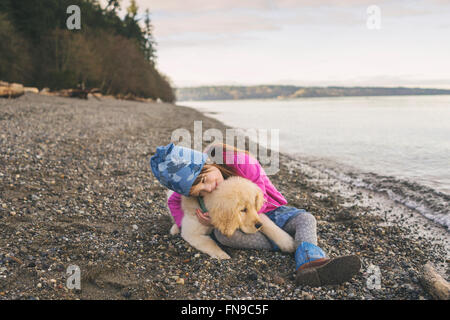 Young girl cuddling with golden retriever puppy on the beach