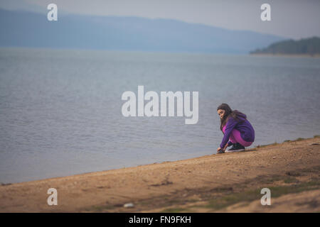 Girl crouching by a lake Stock Photo