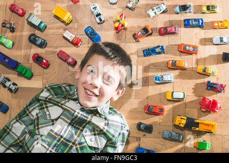 Boy lying on floor surrounded by toy cars Stock Photo