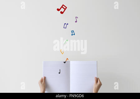 Woman holding notebook with musical notes flying off page Stock Photo
