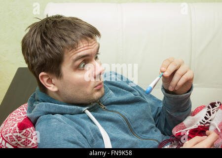 Ill man checking temperature, lying on sofa Stock Photo