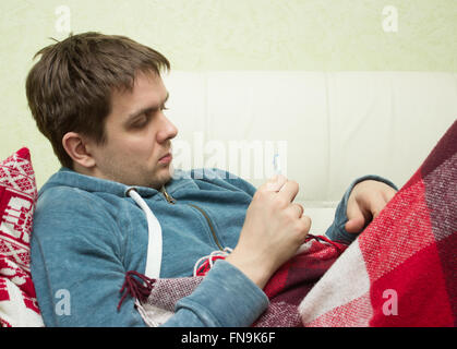 Ill man checking temperature, lying on sofa Stock Photo