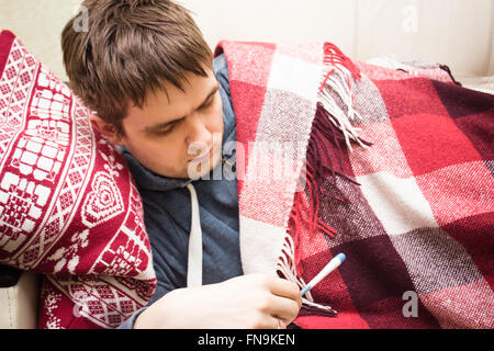 Ill man checking temperature, lying on sofa Stock Photo