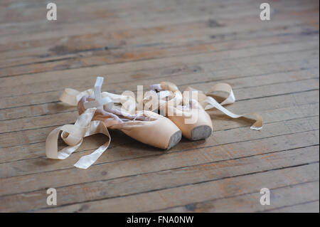 Used pointe shoes on old  wooden floor in dance studio. Concept of classical ballet and modern dance. Shot close-up. Stock Photo