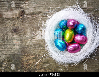 Chocolate eggs in nest on wooden table, top view Stock Photo
