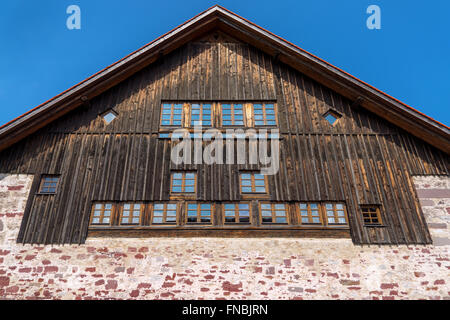 Gable of a rustic house with a dark brown wooden facade above a foundation wall made of red natural stone Stock Photo