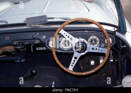Wooden steering wheel and cream coloured/colored instruments on the interior of a vintage British sports car Stock Photo
