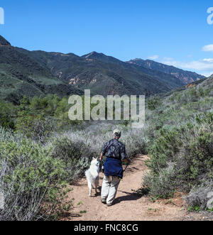Hiker and dog walk down  the ocean view trail at Zuma Canyon Stock Photo