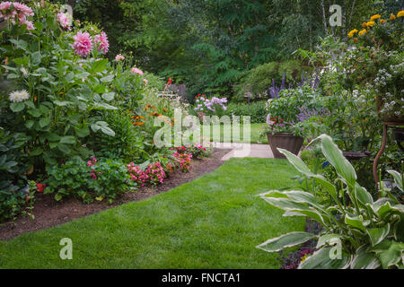 A narrow lawn path leading to a formal backyard garden is flanked by a variety of colorful flowers. Stock Photo