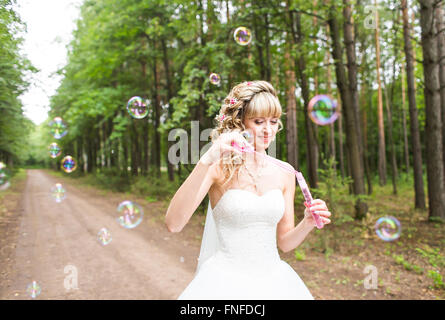 beautiful young woman with white wedding dress blowing bubble outdoors Stock Photo
