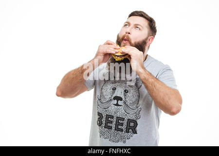 Excited handsome man with beard eating hamburger and enjoying over white background Stock Photo