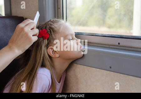 sad six year old girl looking in the window while sitting in an electric train until my mother combs her long hair Stock Photo