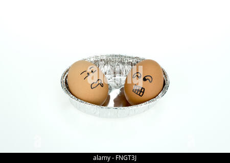 Two eggs with funny faces on oval foil tray, isolated on white background Stock Photo