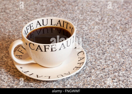 A large round cup of black coffee on a matching saucer on a granite worktop Stock Photo
